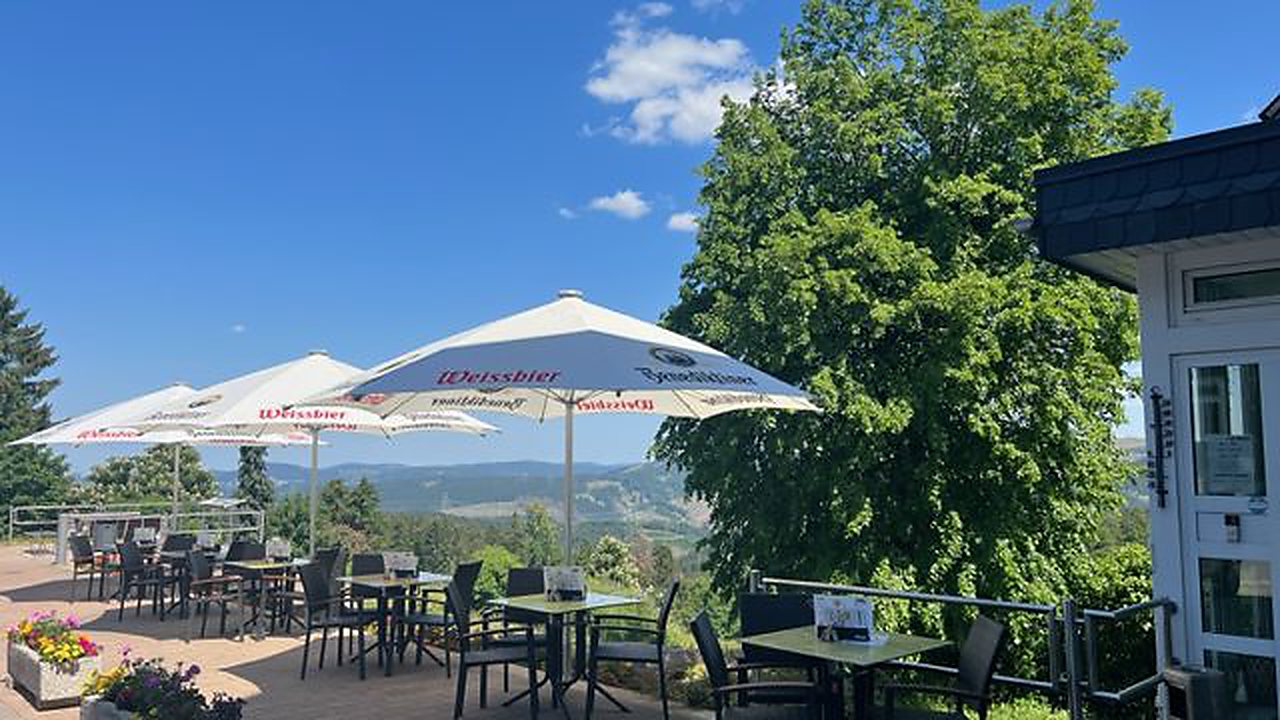 Terrasse der Pizzaheros mit Sonnenschirmen und Blick über die bewaldeten Höhenzüge des Thüringer Waldes