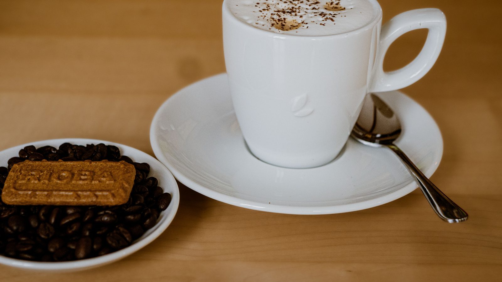Tasse Cappuccino mit Gebäck und Kaffeebohnen auf einem Holztisch