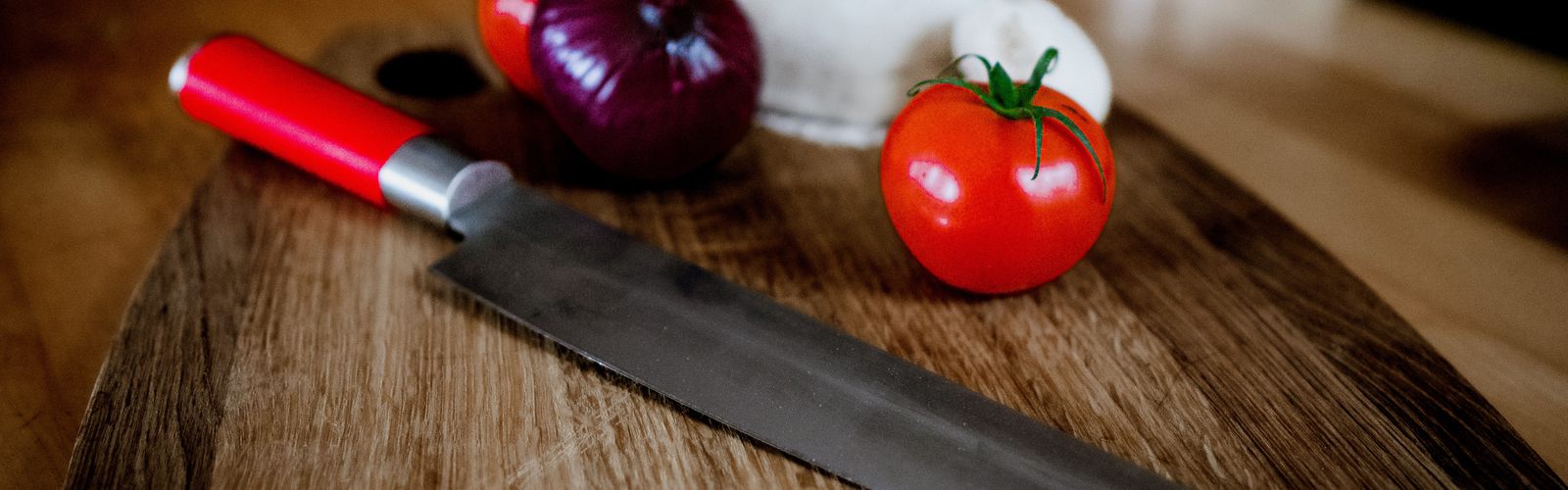 Tomate, rote Zwiebel und Mozzarella neben einem Küchenmesser auf einem hölzernen Schneidbrett